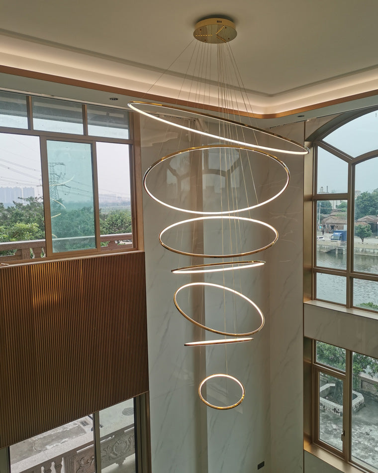 Lit entryway chandelier descending through a window-lined stairwell, using adjustable suspension heights to complement the architecture.