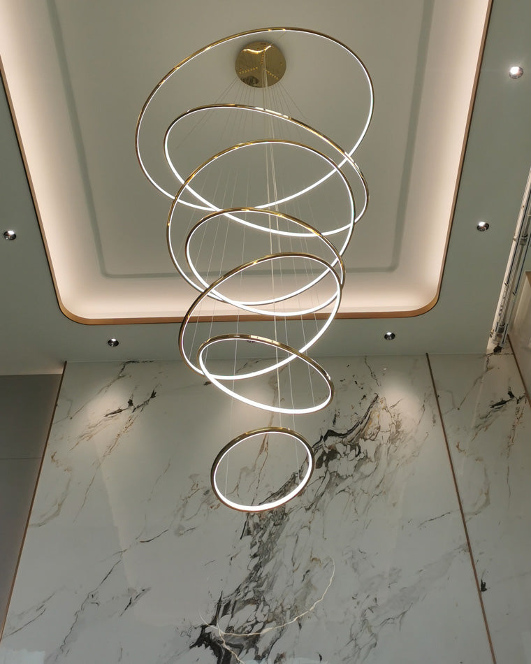 Seven-ring gold chandelier illuminating a marble foyer, using staggered circles to add depth without visually closing the space.
