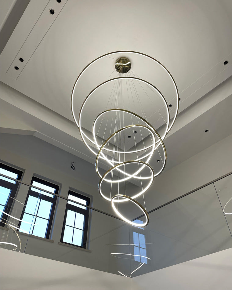 Glowing entryway chandelier suspended through a bright stair void, connecting the upper landing and lower floor with continuous light.