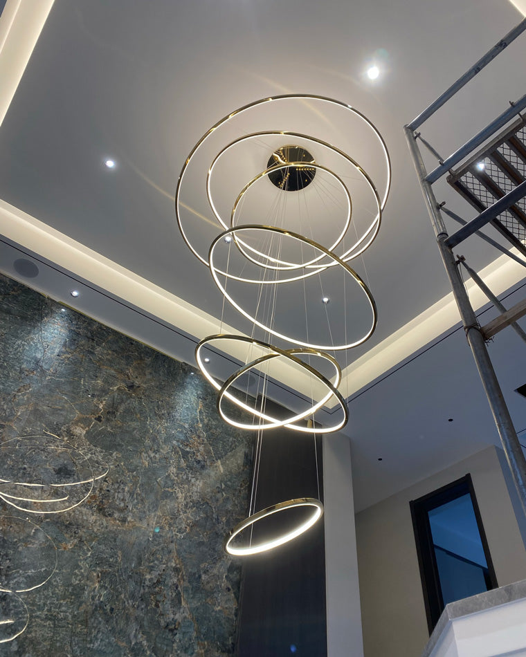 Installed entryway chandelier glowing beside a stone feature wall, transforming a tall stairwell even before the interior is fully finished.