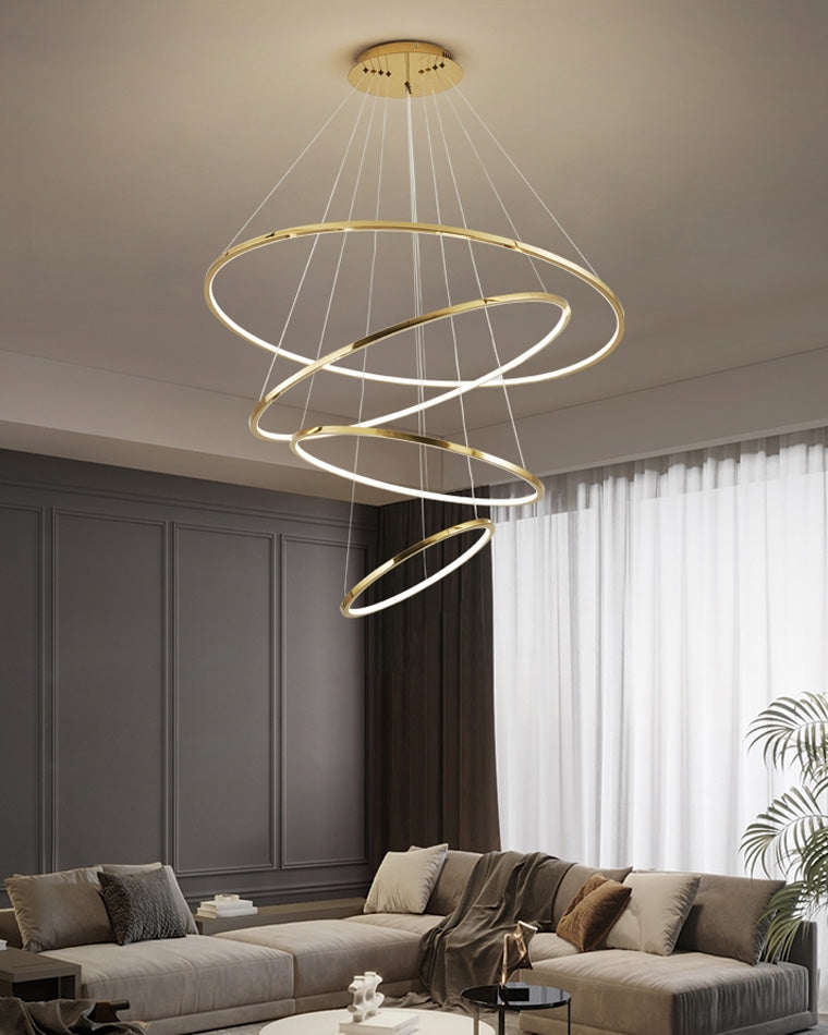 Four illuminated gold rings descending above a gray lounge, delivering statement lighting with a cleaner profile for moderately high ceilings.