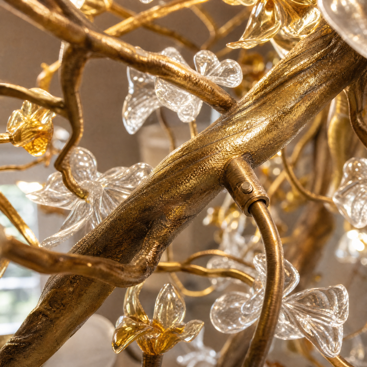 A tall gold cascading chandelier featuring metallic branches and crystal glass blossoms hanging in a high-ceiling space.