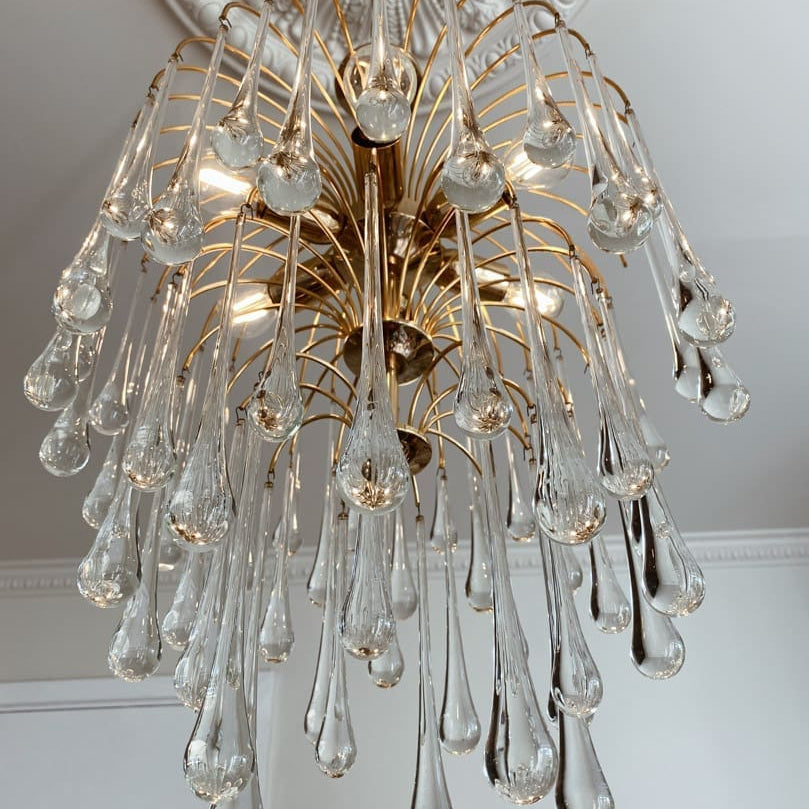 Decorative chandelier with clear glass droplets and gold accents on a white ceiling.