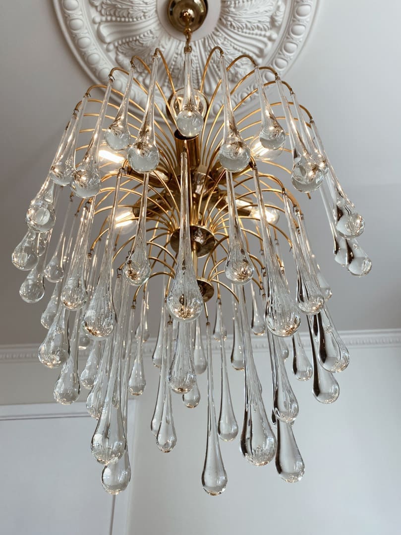 Decorative chandelier with clear glass droplets and gold accents on a white ceiling.