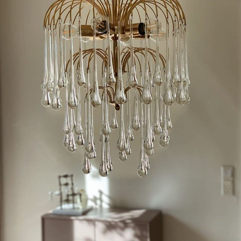 Gold chandelier with clear glass droplets hanging in a room.