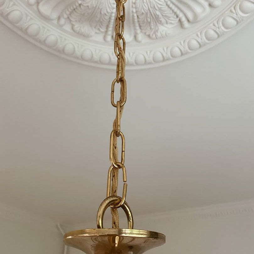 Gold pendant light fixture hanging from a decorative ceiling