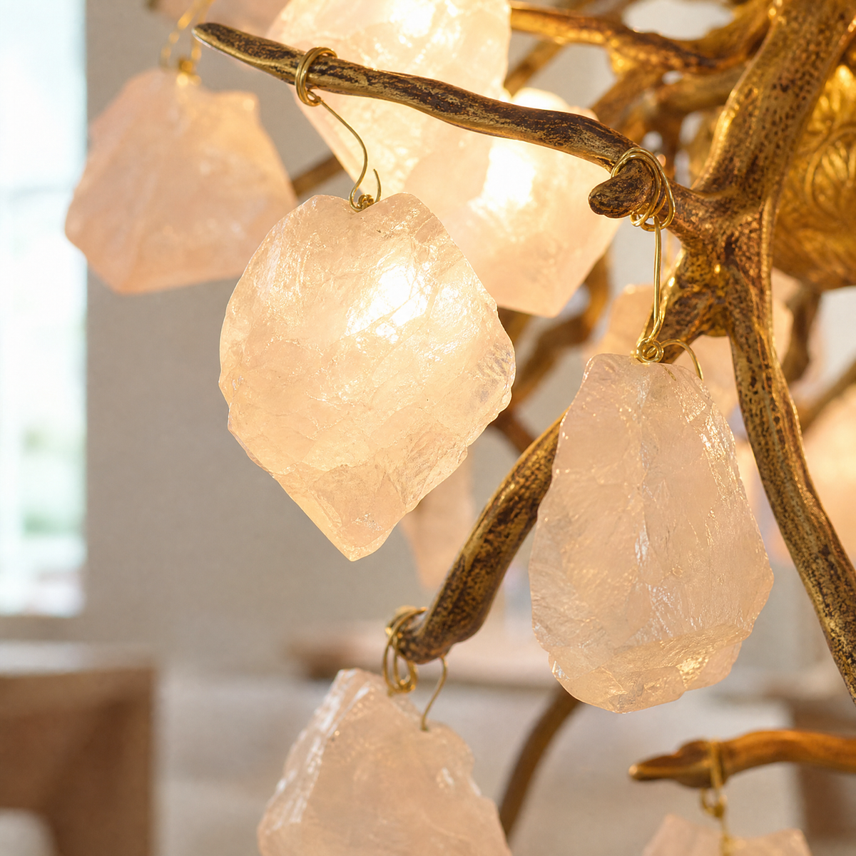 A branching metal chandelier finished in warm brass featuring clusters of raw rose quartz crystals.