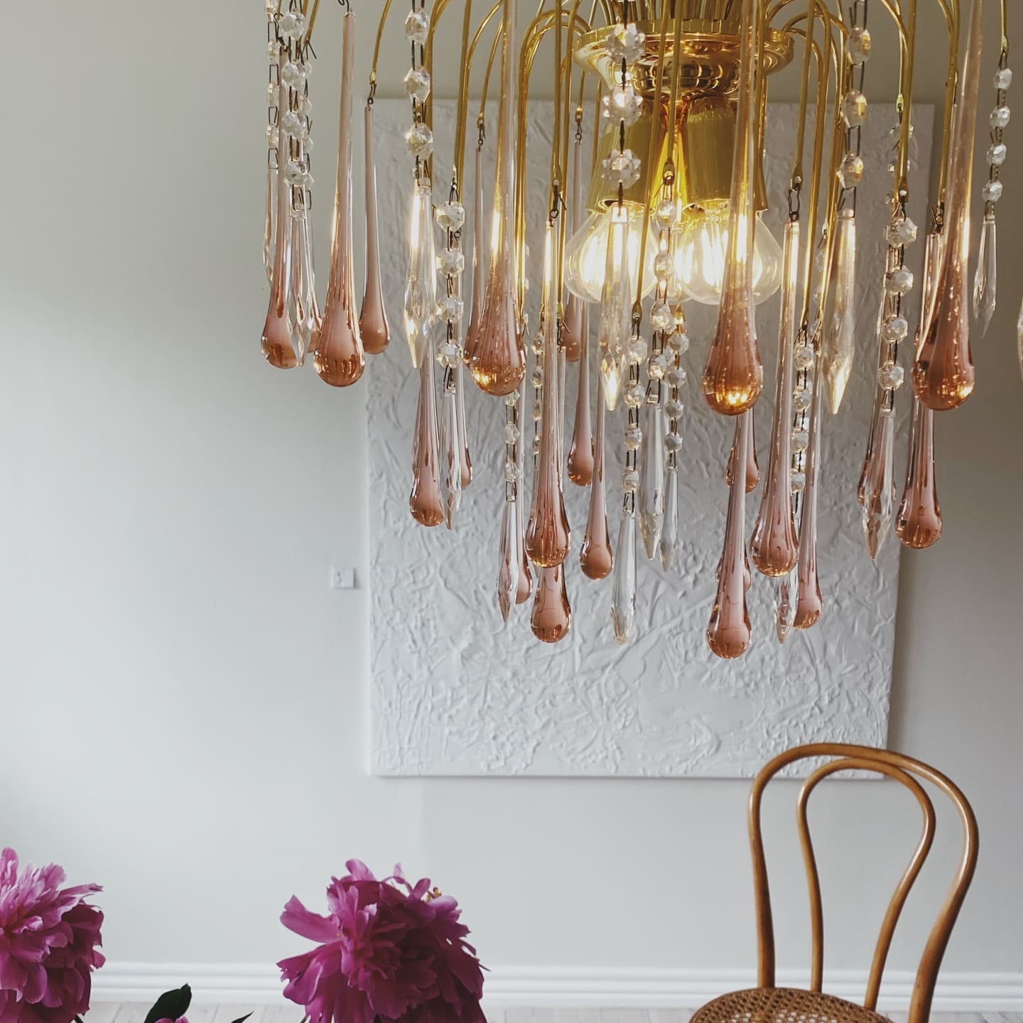 Gold chandelier with crystal-like droplets in a room with a table and chairs.
