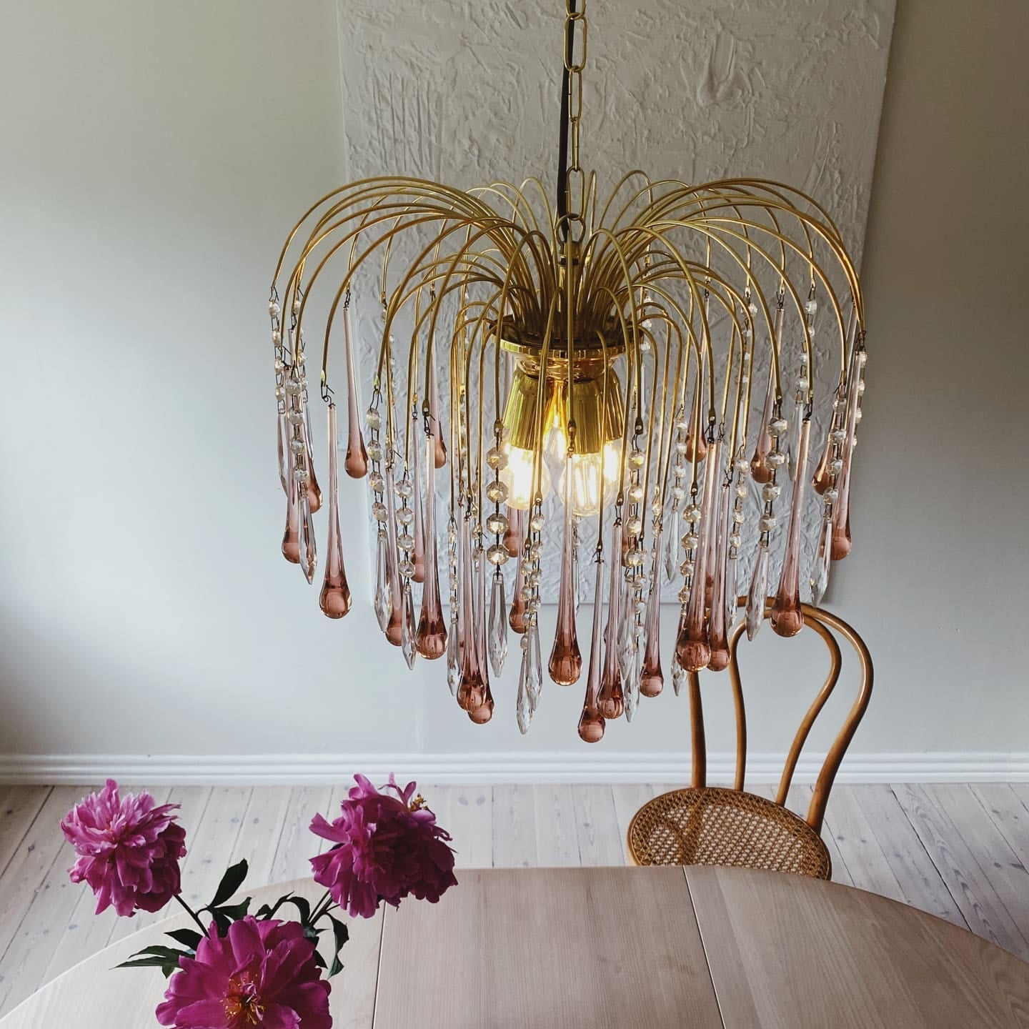 Gold chandelier with glass droplets above a wooden table with pink flowers.