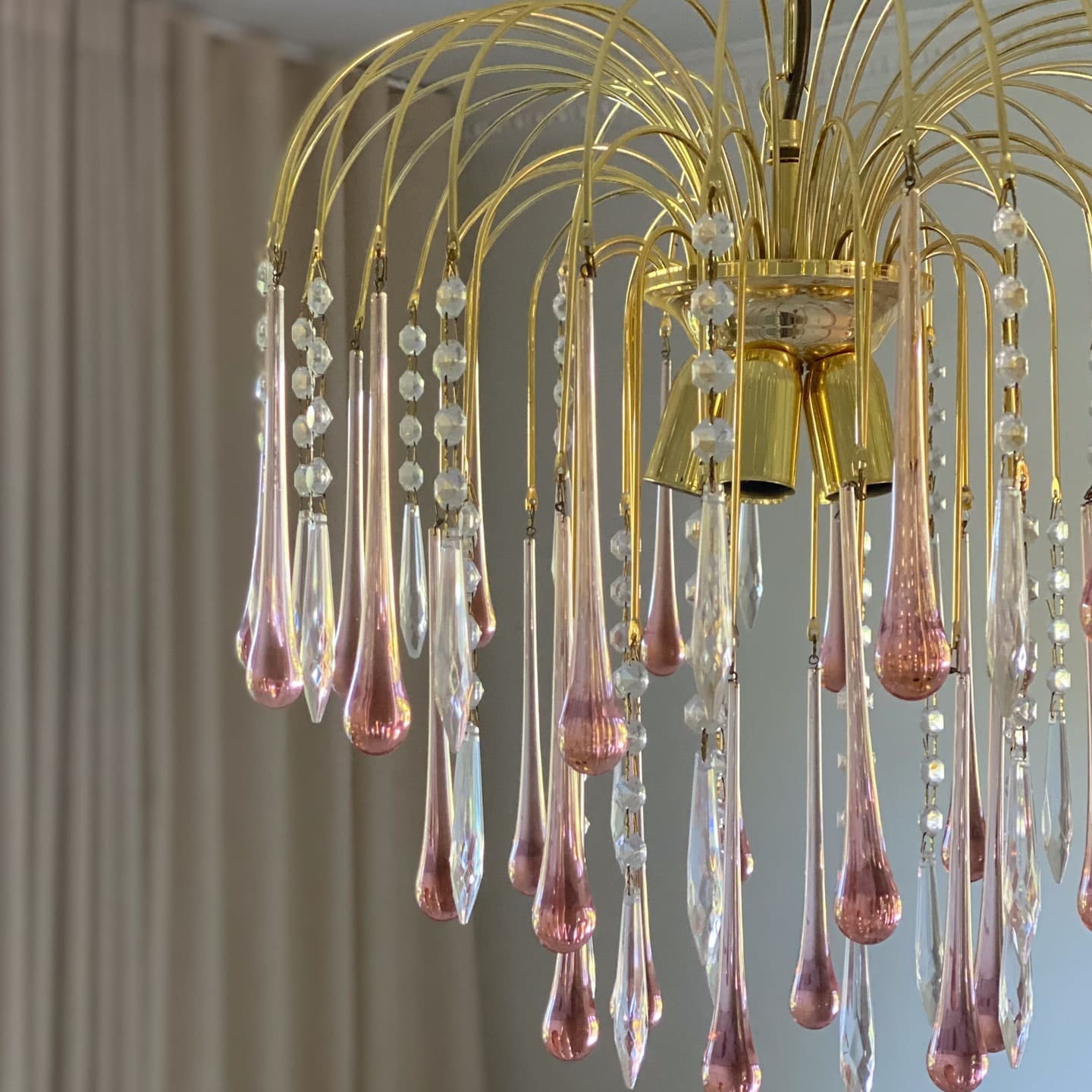 Gold chandelier with pink and clear glass droplets against a neutral background