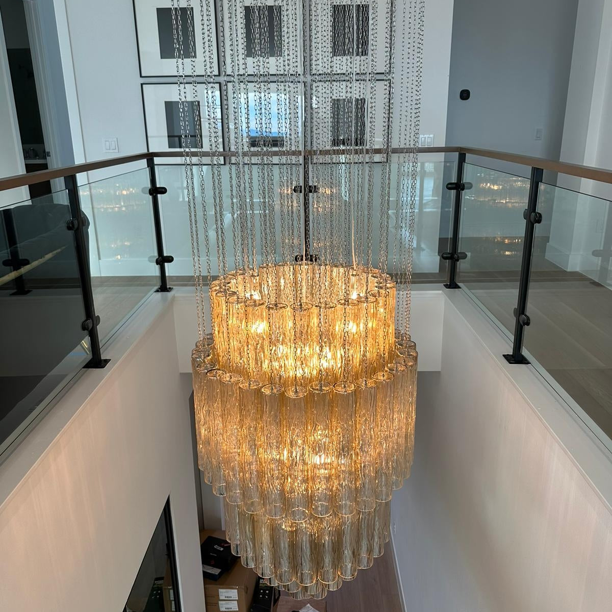 Large chandelier hanging in a modern indoor setting with glass panels and a staircase.