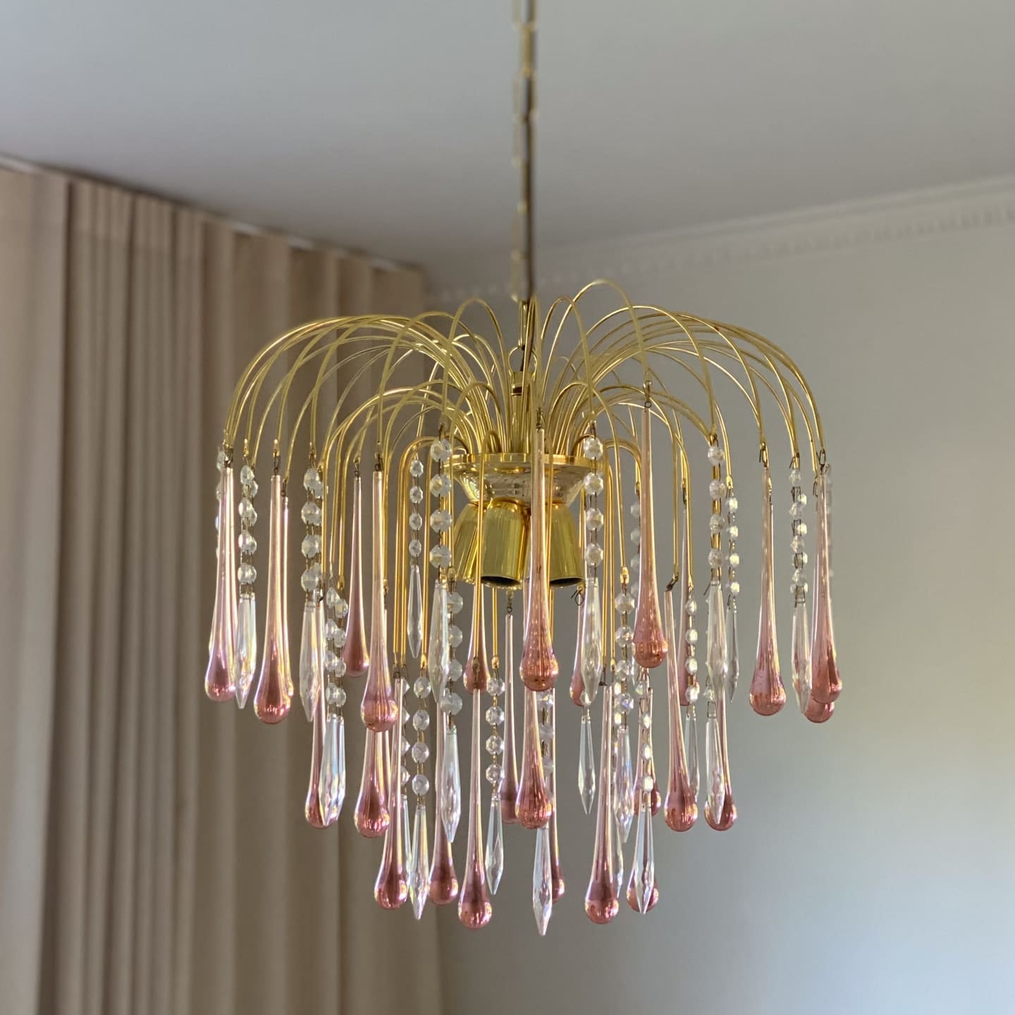 Gold chandelier with pink glass droplets hanging in a room.