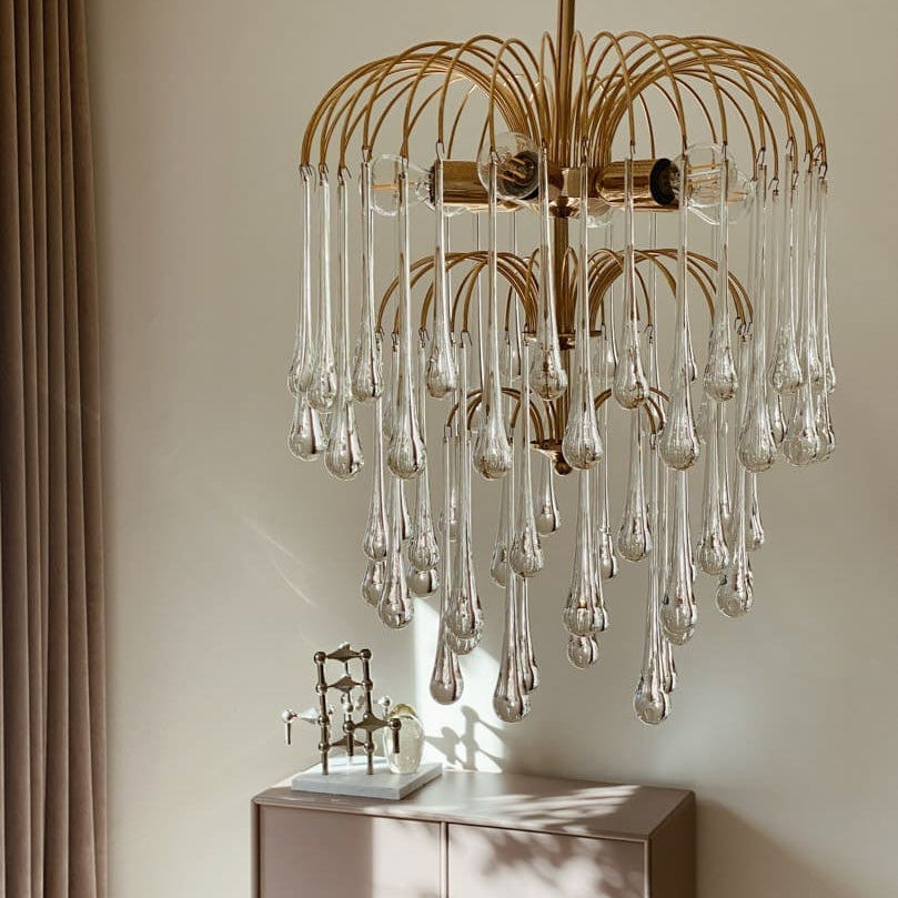 Gold chandelier with clear glass droplets hanging above a cabinet.