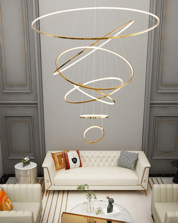 Illuminated gold ring chandelier floating above a formal lounge, filling the tall wall with warm light and a sense of architectural movement.