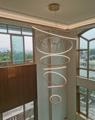 Lit entryway chandelier descending through a window-lined stairwell, using adjustable suspension heights to complement the architecture.