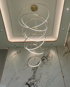 Seven-ring gold chandelier illuminating a marble foyer, using staggered circles to add depth without visually closing the space.