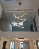 Long gold ring chandelier installed through a two-story opening, demonstrating how its adjustable drop can suit challenging ceiling heights.