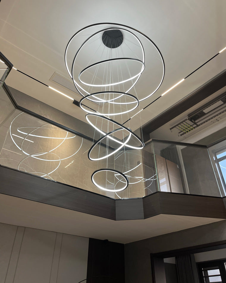 Shiny black entryway chandelier glowing above a mirrored stairwell, combining graphic contrast with airy, unobstructed sightlines.