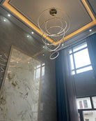 Warm gold rings descending beside a double-height window, adding softness and human scale to an otherwise imposing interior.