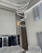 Long illuminated chandelier above a double-height seating area, distributing light vertically instead of leaving the upper space dark.
