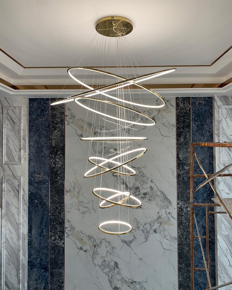 Fully illuminated gold ring chandelier against a marble feature wall, creating a luxurious centerpiece during the final installation stage.