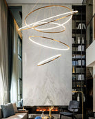 Sculptural entryway chandelier suspended beside a floor-to-ceiling library and fireplace, making the tall interior feel composed rather than empty.