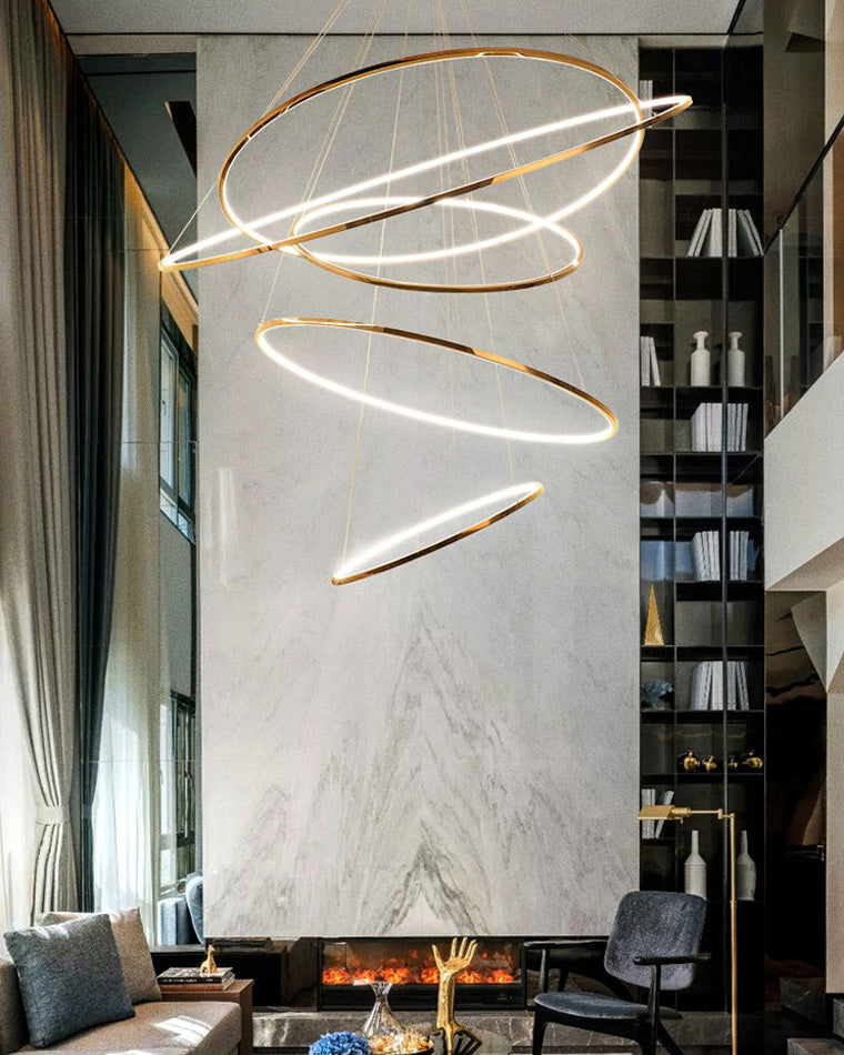 Sculptural entryway chandelier suspended beside a floor-to-ceiling library and fireplace, making the tall interior feel composed rather than empty.
