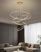 Four illuminated gold rings descending above a gray lounge, delivering statement lighting with a cleaner profile for moderately high ceilings.