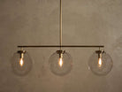 Front view of a brass chandelier with three clear glass globe shades, each containing an illuminated filament bulb.