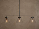 Front view of a black linear pendant light fixture with three clear conical glass shades and exposed warm Edison bulbs.