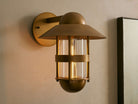 Illuminated Hyannis Outdoor Sconce, antique brass, nautical style with glass housing and visible bulb, on a light wall.