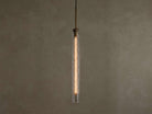 Vertical view of a lit pendant light with a clear textured glass cylinder, a warm filament bulb, and a brass-colored top fixture.