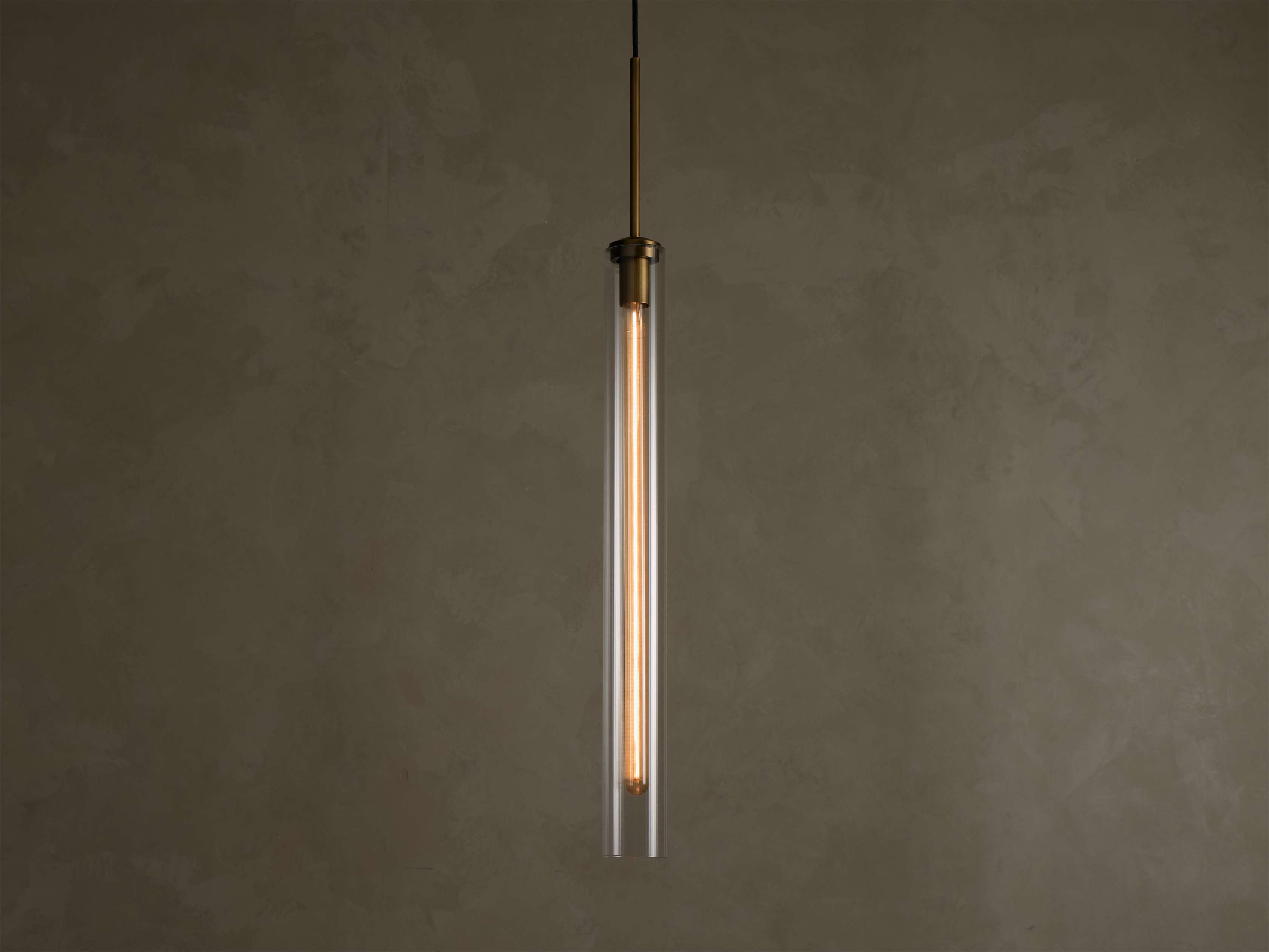 Front view of a modern brass and clear glass pendant light fixture with a long, illuminated filament bulb inside.