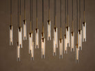 Multiple illuminated pendant lights with clear glass tubes and brass fixtures, hanging at varying heights from black cords.