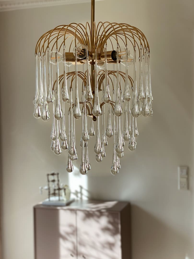 Gold chandelier with clear glass droplets hanging in a room.