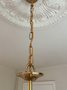Gold pendant light fixture hanging from a decorative ceiling