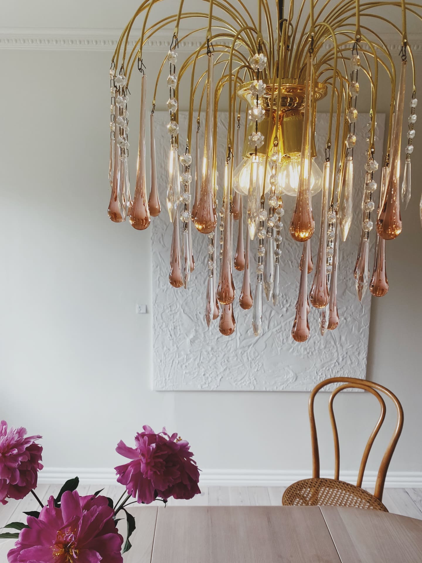 Gold chandelier with crystal-like droplets in a room with a table and chairs.