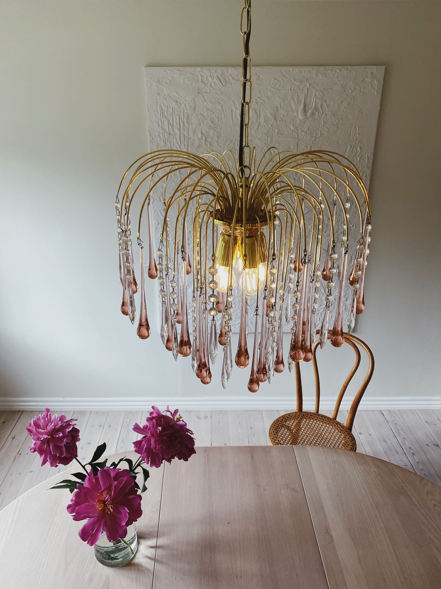 Gold chandelier with glass droplets above a wooden table with pink flowers.