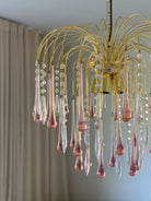 Gold chandelier with pink and clear glass droplets against a neutral background