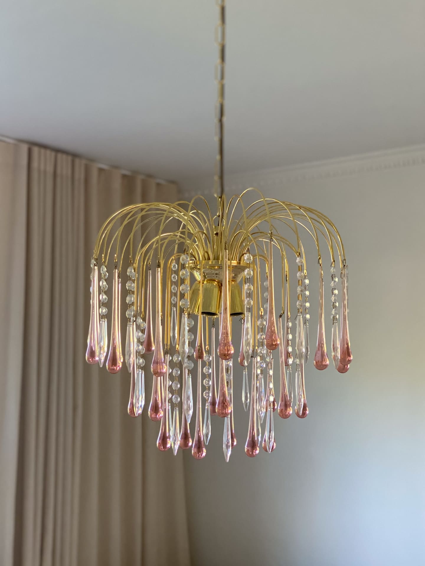 Gold chandelier with pink glass droplets hanging in a room.